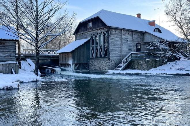 The wooden Ginučiai watermill with its water wheel turning beside a forest stream